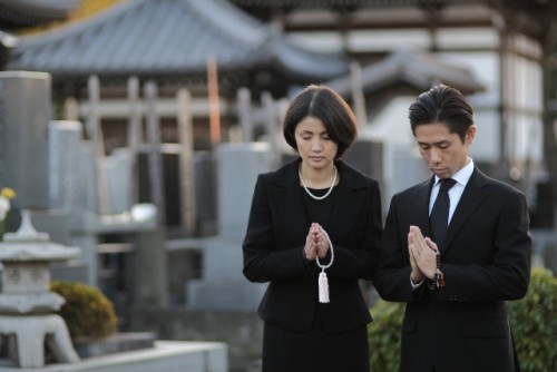 お墓で手を合わせr喪服のカップル